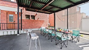 An outdoor patio with a brick wall, a covered area with a green roof, and a table set for a meal. - BRIC (Asahikawa)