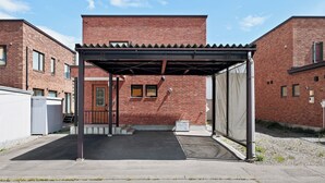 A covered parking area with a brick building in the background. - BRIC (Asahikawa)