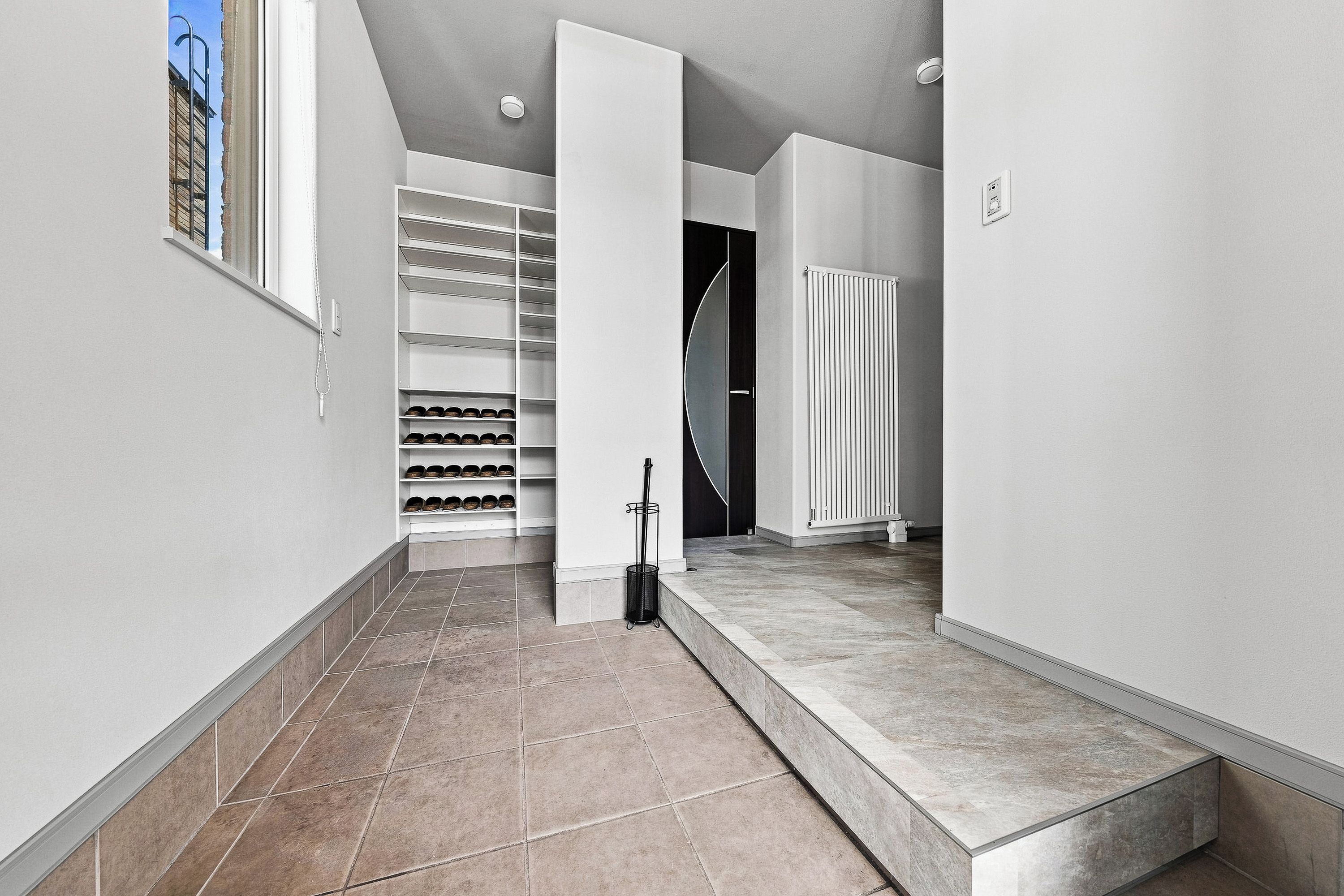 A modern interior with a tiled floor, a shoe rack, and a radiator.