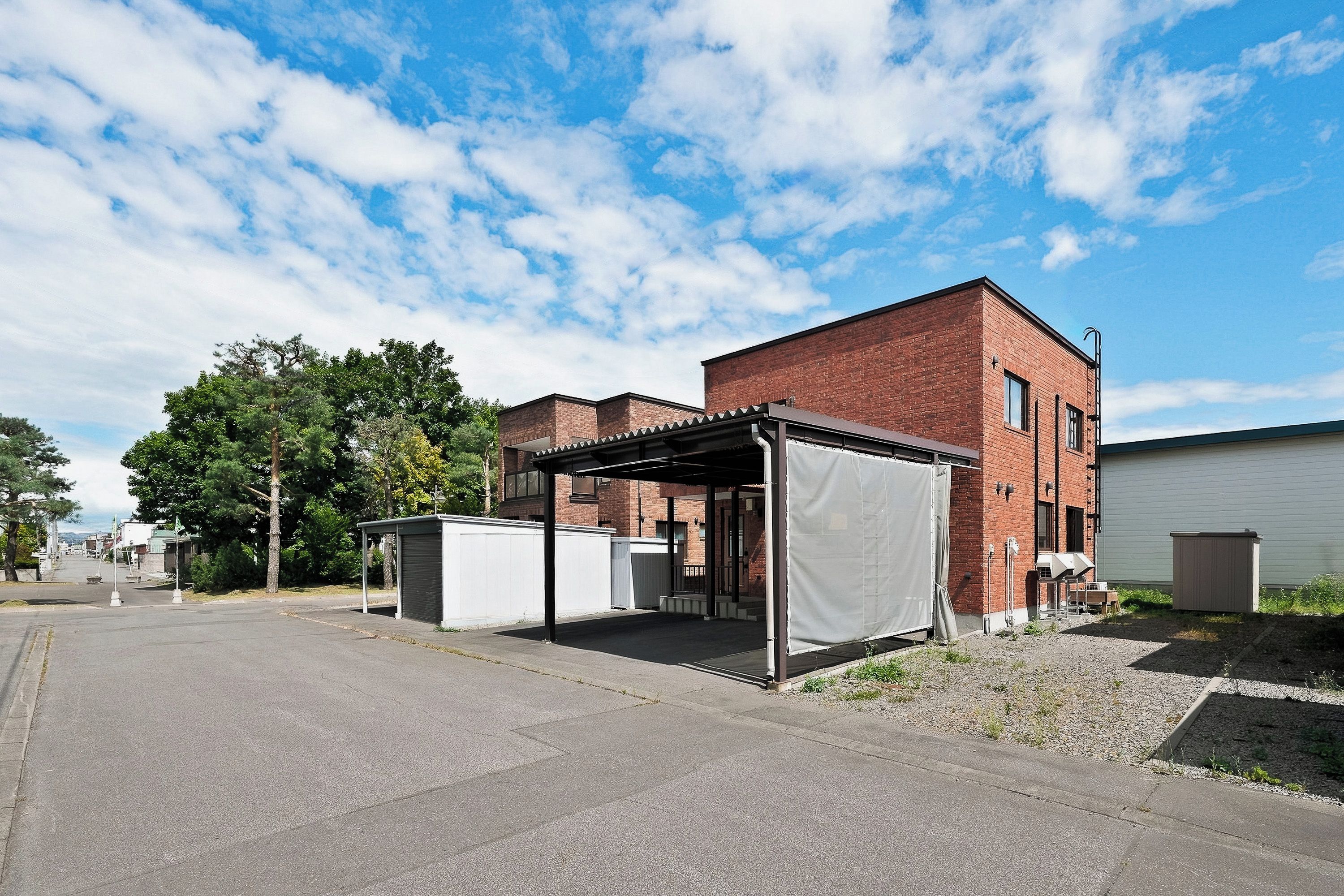 A parking area with a covered shelter, a brick building, and a clear sky.