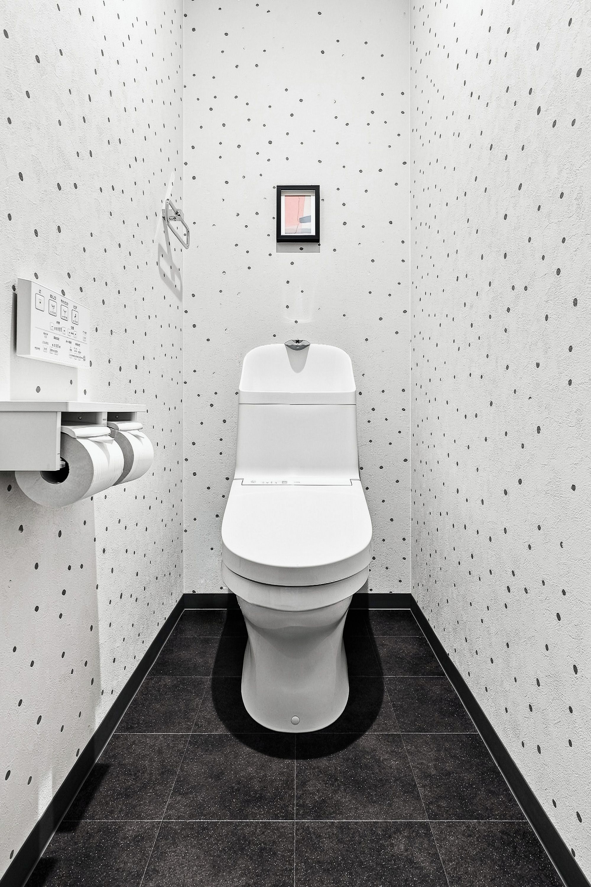 A compact, modern bathroom with a toilet, a hand dryer, and a small framed picture on the wall.