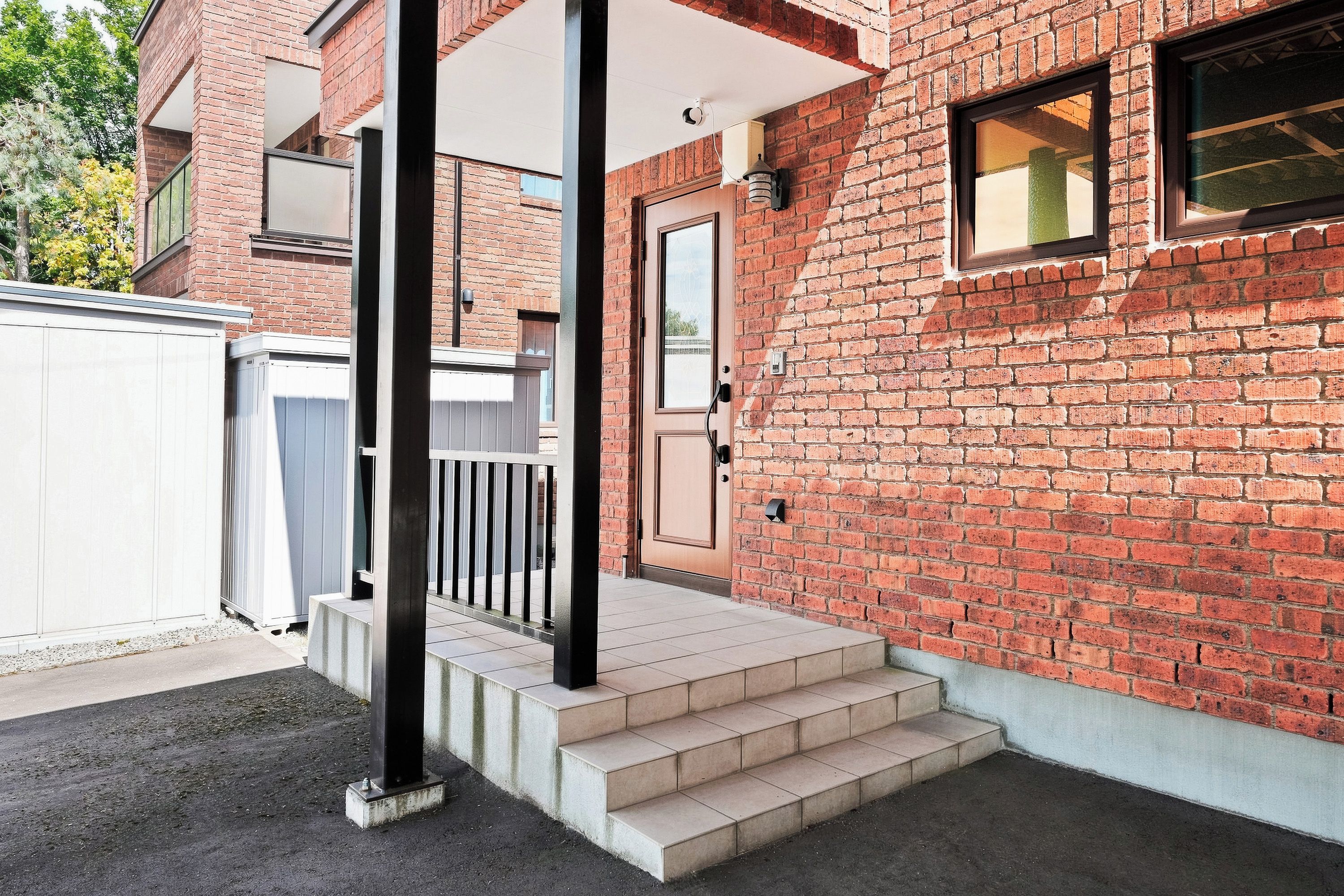A brick building with a front door, a small porch with steps, and a white fence.