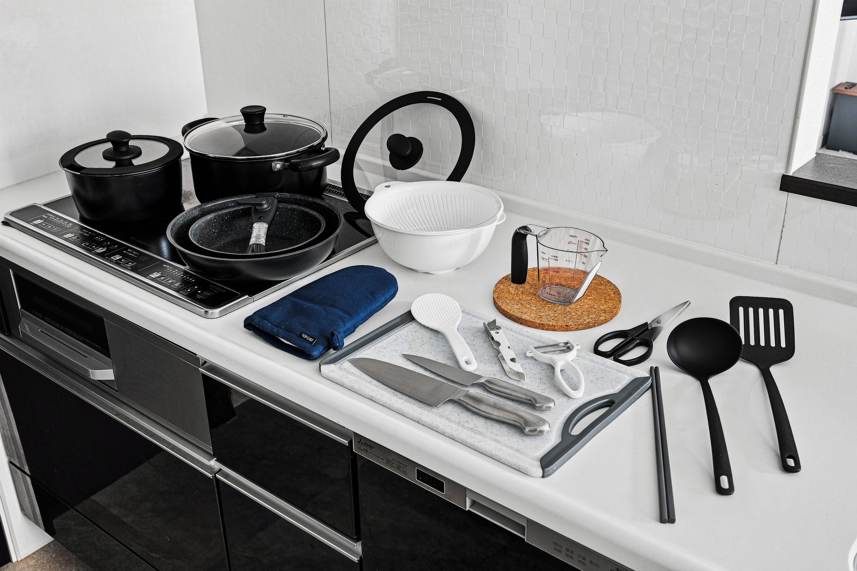 A kitchen counter with various cooking utensils, a pot, a pan, a colander, and a measuring cup.