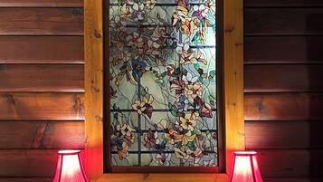 A wooden-framed stained glass window with floral patterns, flanked by two table lamps on a white cabinet.