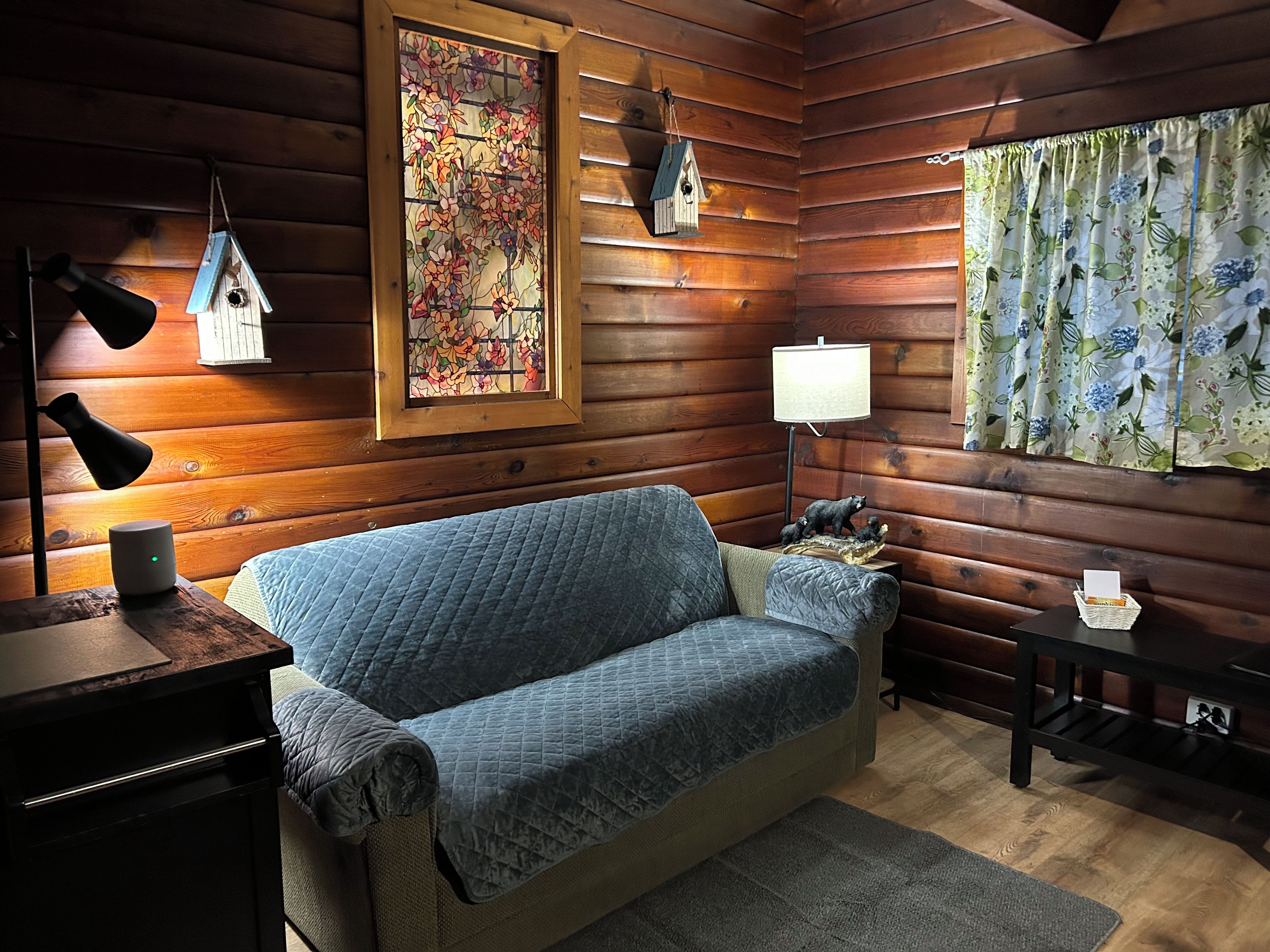 L’intérieur d’un chalet chaleureux, avec un canapé matelassé, un mur en bois, un vitrail et une lampe.
