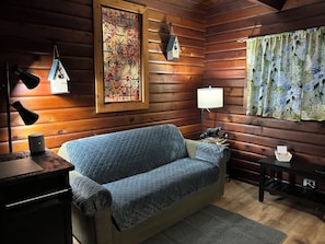 Interior acogedor de una cabaña con un sofá acolchado, una pared de madera, un vitral y una lámpara.