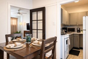A dining area with a wooden table set for two, a kitchen with modern appliances, and a ceiling fan. - Lakeview 1BR Apt Near Wrigley & Lake Michigan (Chicago)
