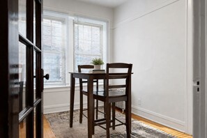 A room with a dining table and chairs, a potted plant, and a window with blinds. - Lakeview 1BR Apt Near Wrigley & Lake Michigan (Chicago)