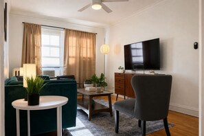 A living room with a sofa, a chair, a TV, a lamp, and a small table with a plant. - Lakeview 1BR Apt Near Wrigley & Lake Michigan (Chicago)