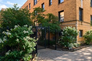A brick building with a gated entrance, surrounded by greenery and flowering plants. - Lakeview 1BR Apt Near Wrigley & Lake Michigan (Chicago)