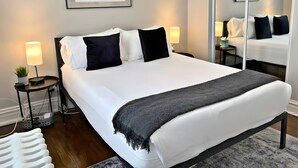 Habitación de hotel moderna con una cama grande, dos mesitas de noche, un espejo y una obra de arte abstracta en la pared.