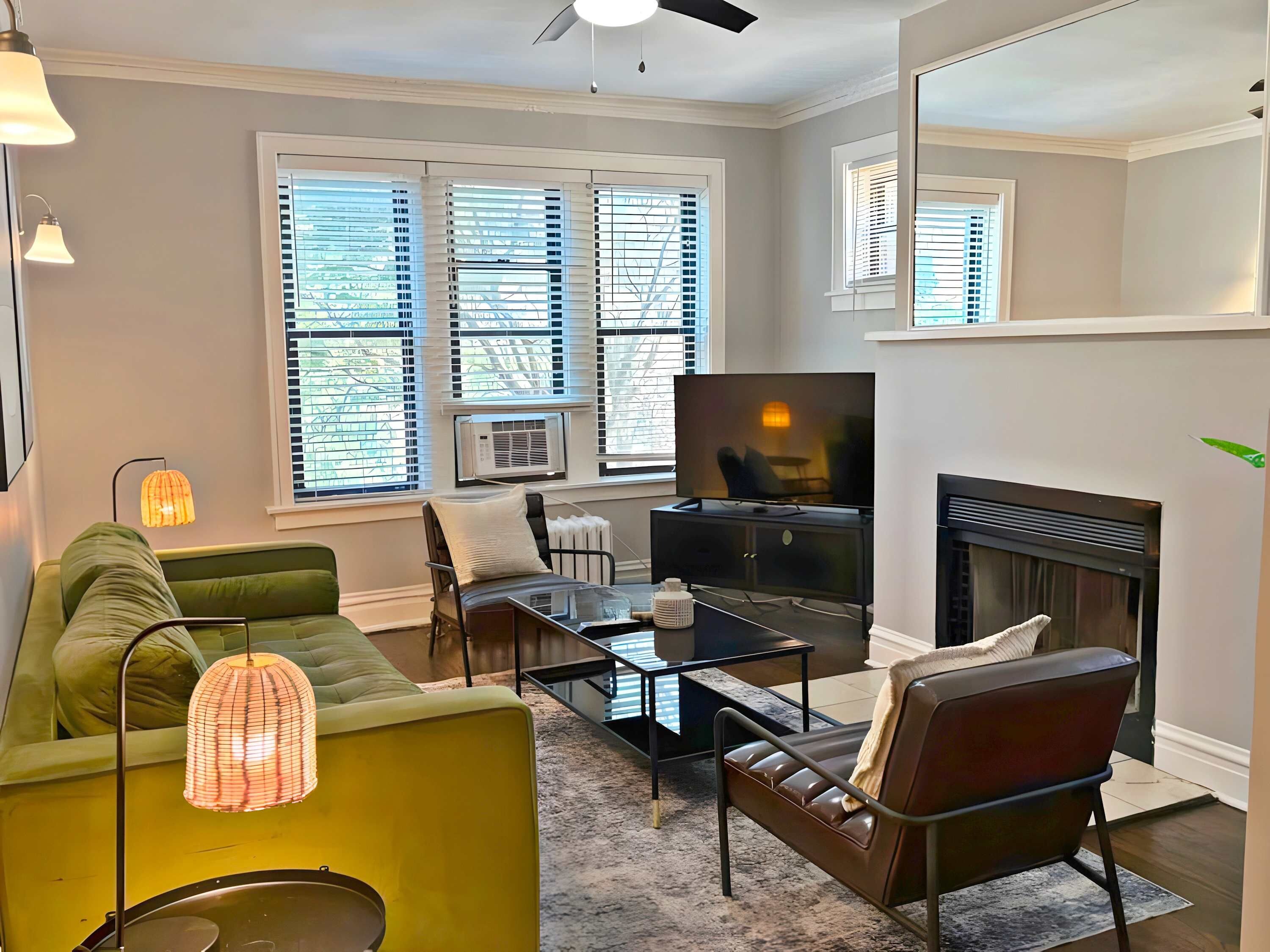A living room with a green sofa, a leather armchair, a coffee table, a flat-screen TV, and a fireplace.