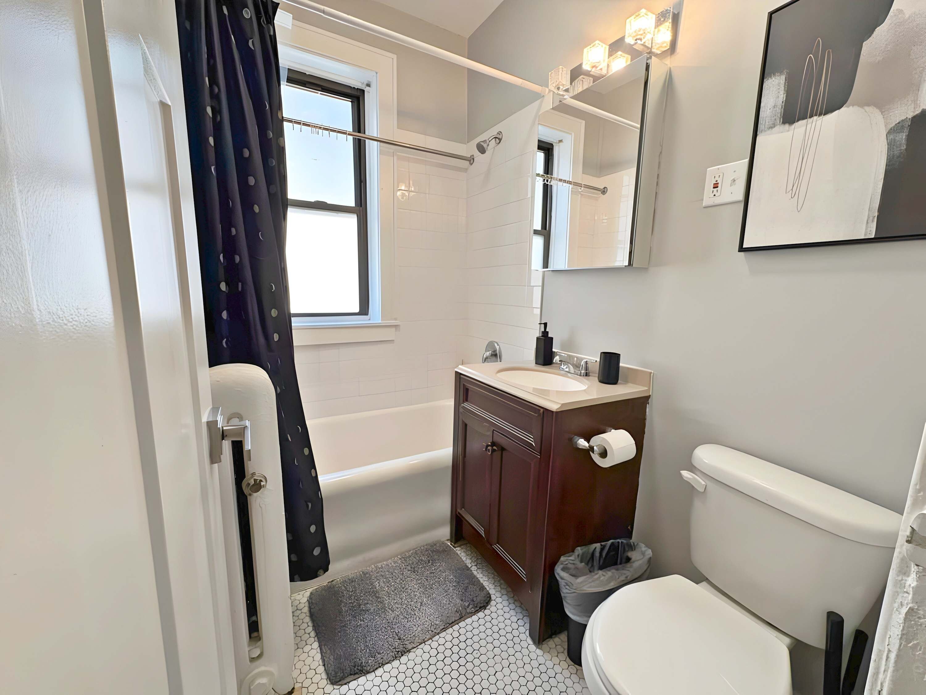 A bathroom with a bathtub, toilet, sink, and a mirror with lights.