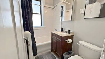 A bathroom with a bathtub, toilet, sink, and a mirror with lights.