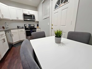 A modern kitchen with white cabinets, a microwave, stove, and oven. There is a dining table with two chairs and a potted plant. - Smart & Stylish 2-Bedroom Unit (Chicago)