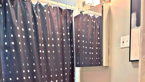 Un baño con una cortina oscura con estampado de luna creciente blanca, un tocador de madera con encimera color beige, un inodoro blanco y un espejo pequeño sobre el lavabo.