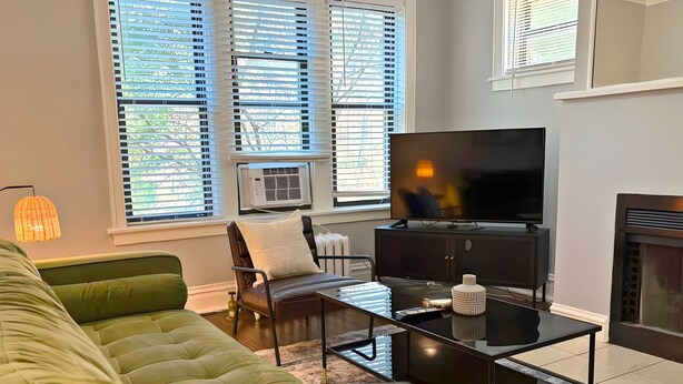 Una sala de estar con un sofá verde, una mesa de centro negra, un televisor y una chimenea.