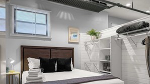 En pænt redt seng med hvide og sorte puder, en sengetavle og et lille bord med lampe.