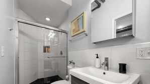 Et moderne badeværelse med en glas brusekabine, et hvidt toilet, en vask med spejl og en sort bordplade.