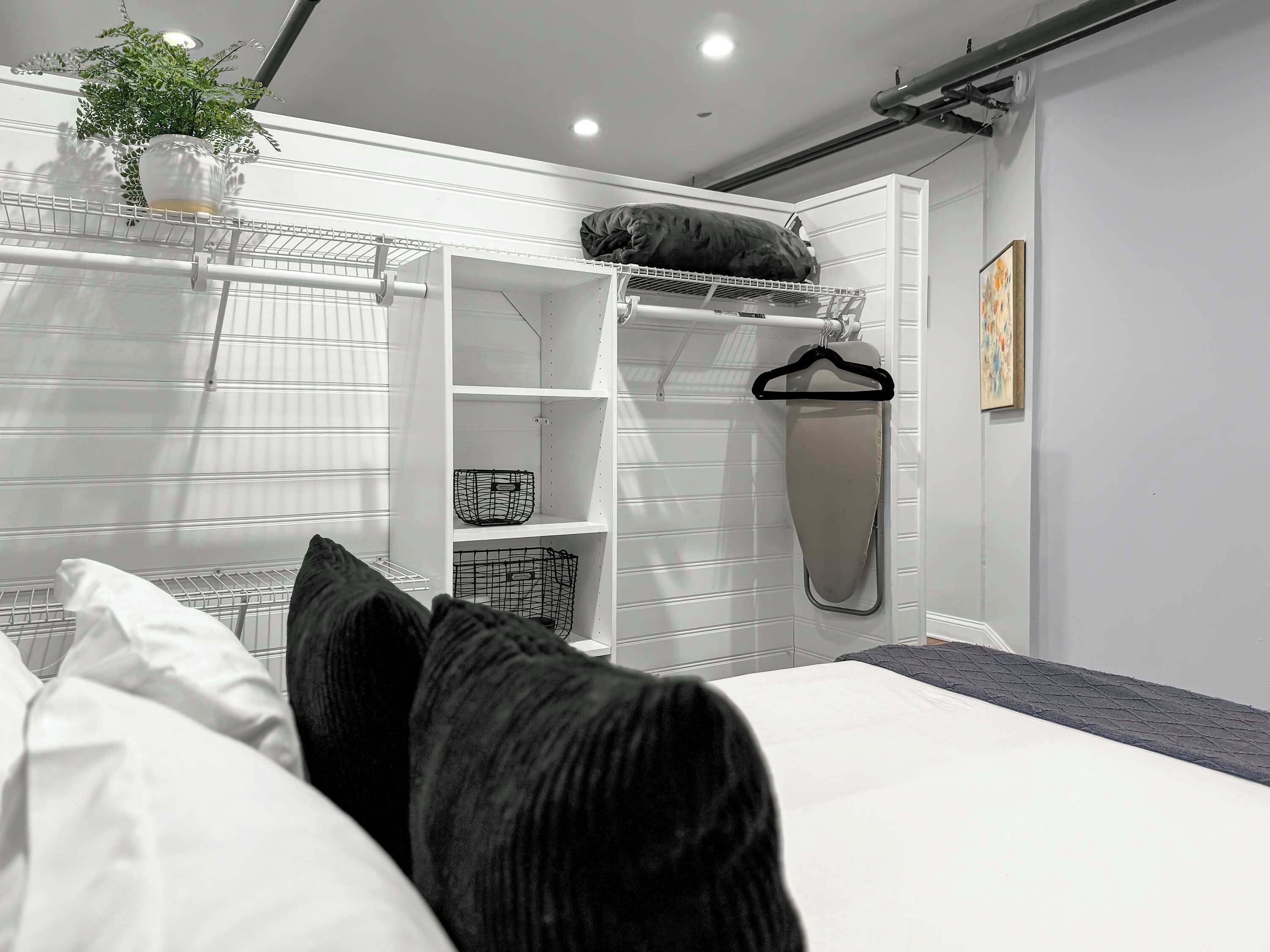 Een moderne slaapkamer met een bed, witte muren en een hangplant.