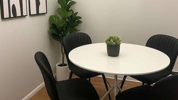 A round table with four black chairs, a potted plant, and a piece of abstract art on the wall.