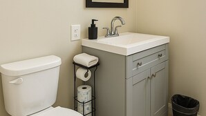 Een badkamer met een toilet, een wastafel met een spiegel erboven, een handdoekhouder en een prullenbak.