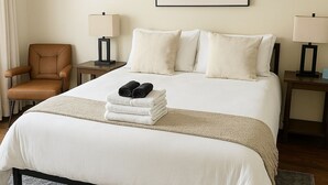Een hotelkamer met een bed, een stoel, twee nachtkastjes en een ingelijst beeld aan de muur.