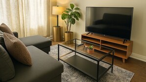 Een moderne woonkamer met een bank, een glazen salontafel, een flatscreen televisie, een lamp en een potplant.