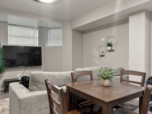 A modern living room with a sofa, a wooden dining table, and a TV mounted on the wall.