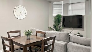 Ein Wohnzimmer mit Esstisch, Stühlen, einer Couch, einem Fernseher und einer Wanduhr.