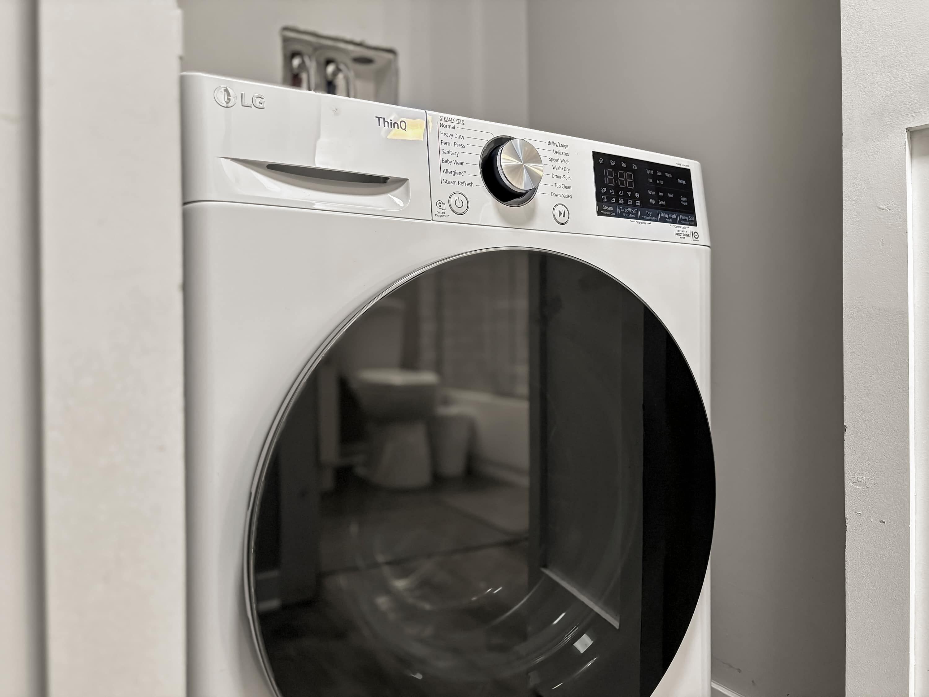 A front view of a white LG ThinQ washing machine with a control panel and a circular door.