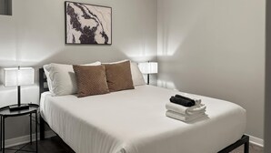 Ein Hotelzimmer mit einem Bett, zwei Nachttischlampen, einem Wandbild und einem kleinen Tisch mit einer Lampe.