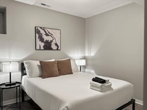 Een hotelkamer met een bed, twee bedlampen, een kunstwerk aan de muur en een klein tafeltje met een lamp.