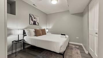 Een slaapkamer met een bed, nachtkastjes, een vloerkleed, een plafondlamp en een kunstwerk aan de muur.