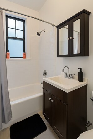 Ein Badezimmer mit Badewanne, Dusche, Waschbecken und einem Spiegel darüber sowie einem Fenster mit Vorhang.