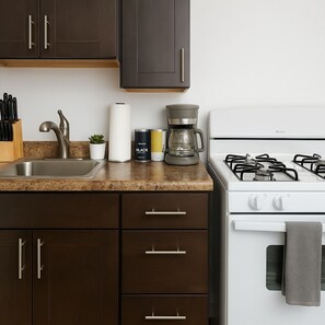 Eine Küche mit einer Edelstahl-Spüle, einer Kaffeemaschine, einem Gasherd und dunkelbraunen Schränken.