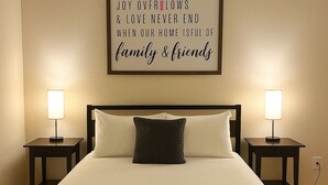 Ein ordentlich bezogenes Bett mit Kissen, zwei Nachttischlampen und einem gerahmten Motivationsspruch an der Wand.