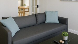 Ein modernes Wohnzimmer mit einem grauen Sofa, einem schwarzen Couchtisch und einem Bild an der Wand.