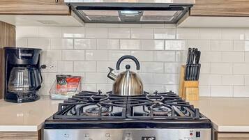 Une cuisine équipée d’une cuisinière à gaz, d’une bouilloire, d’une machine à café et d’un bloc à couteaux.