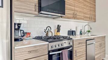 Una cocina moderna con armarios de madera, una estufa de acero inoxidable, un microondas y un lavavajillas.