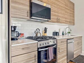 A modern kitchen with wooden cabinets, a stainless steel stove, a microwave, and a dishwasher.