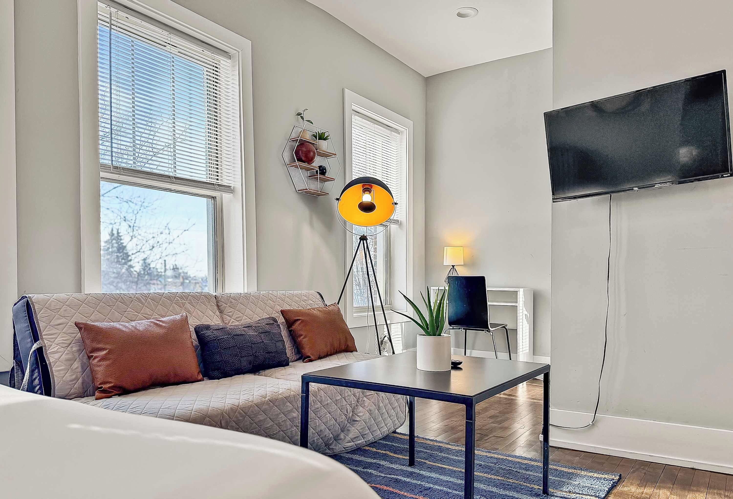 Un salon moderne avec un canapé, une table basse, un lampadaire et un téléviseur à écran plat fixé au mur.