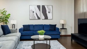 Ett modernt vardagsrum med en blå soffa, en grå soffa och en tv. Det finns två väggmonterade lampor och en växt på ett soffbord.