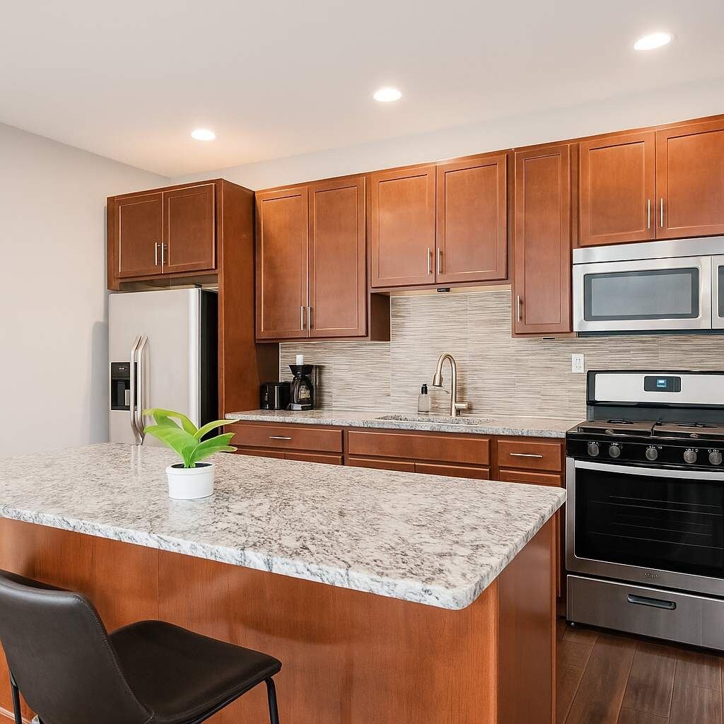 A modern kitchen with wooden cabinets, a granite countertop, a stainless steel refrigerator, a microwave, a coffee maker, and an oven.