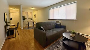 En moderne stue med en grå sofa, et rundt sofabord og et spiseområde med bord og stole.