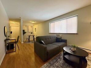 A modern living room with a gray sofa, a round coffee table, and a dining area with a table and chairs.