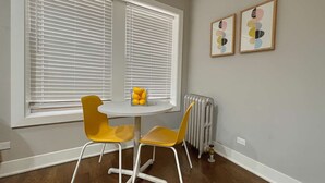 Una habitación con dos sillas amarillas alrededor de una pequeña mesa blanca, un radiador y dos cuadros en la pared.