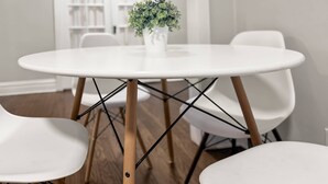 A round white table with a potted plant in the center, surrounded by white chairs with wooden legs.