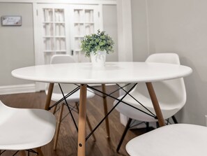 Una mesa redonda blanca con una planta en maceta en el centro, rodeada de sillas blancas con patas de madera.