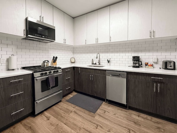 A modern kitchen with dark wood cabinets, white subway tiles, stainless steel appliances, and a wooden floor.